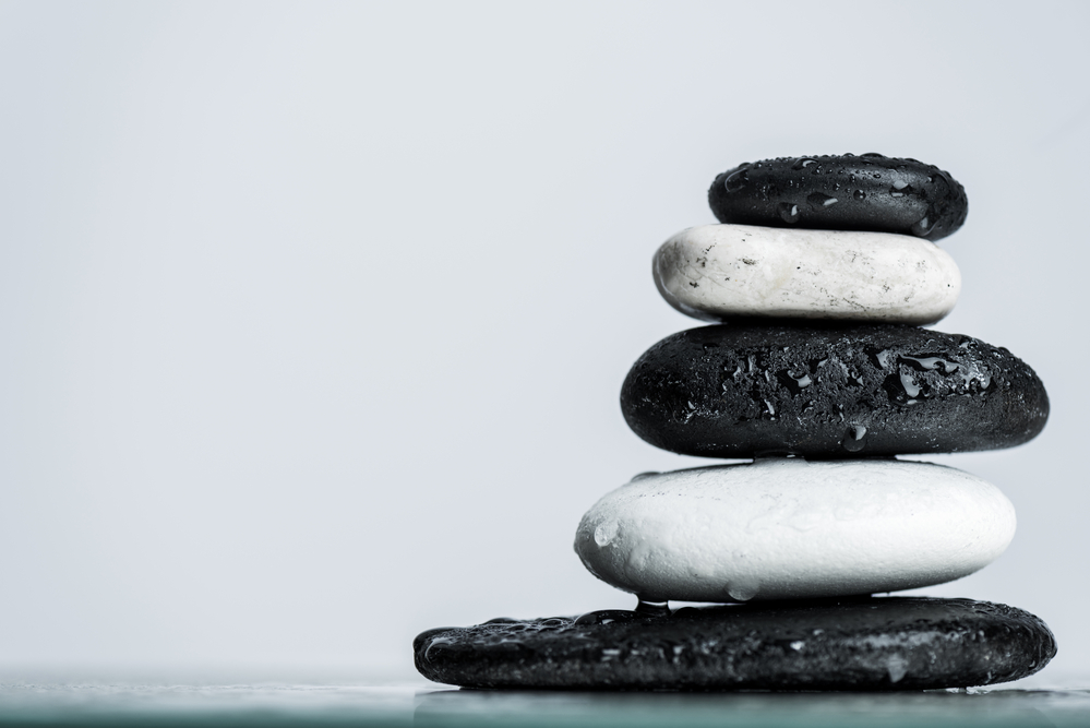 A balanced stack of smooth black and white stones is set against a minimalist, pale background. The stones glisten with droplets of water, evoking a sense of workplace wellness and tranquility.