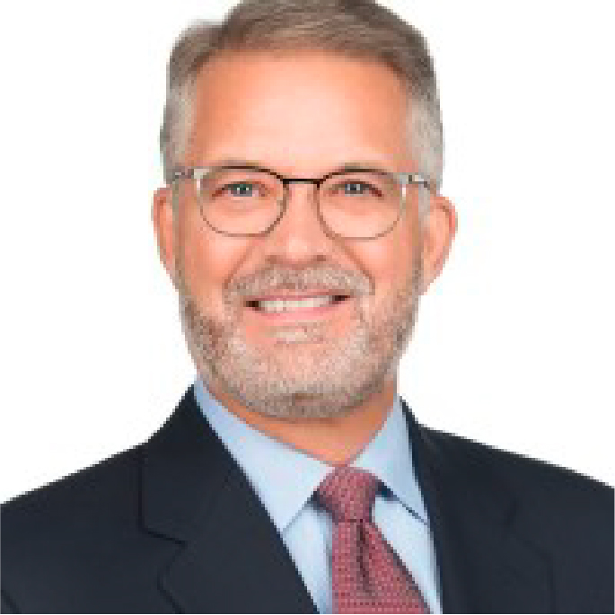 Smiling man with short gray hair and a beard, wearing glasses, a dark suit, light blue shirt, and red tie, stands confidently against a white background. Meet Craig Hohnberger.